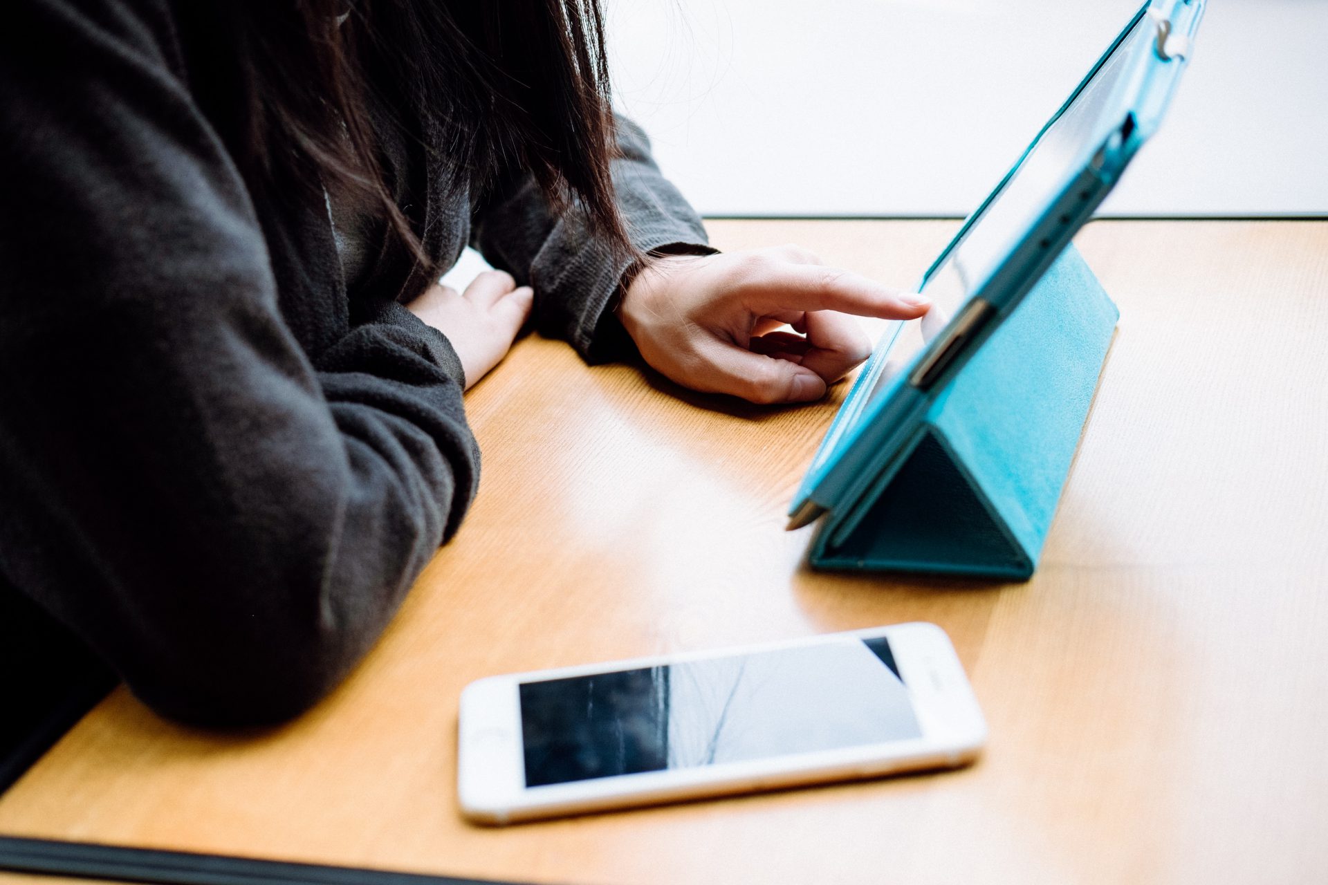 female tapping on ipad with iphone on the desk next to her.