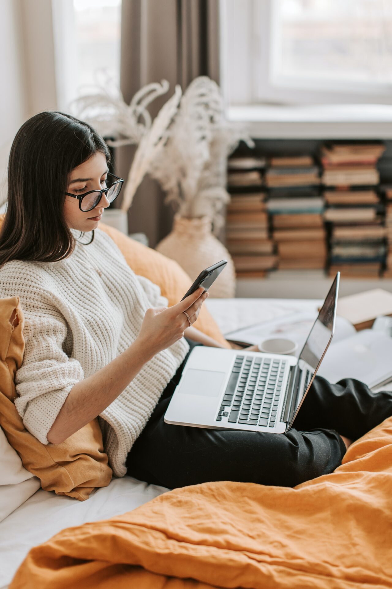 young woman with laptop responding to something on her smartphone